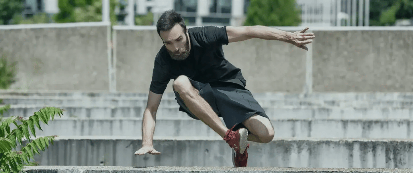 Bearded man jumping over a short wall during parkour